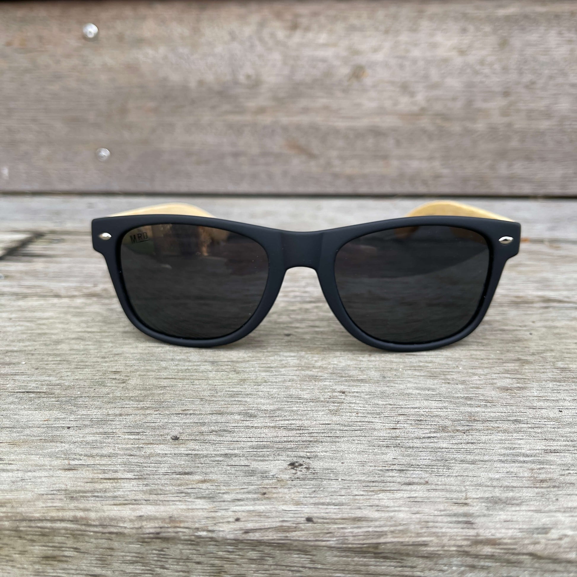 Sunglasses with wooden arms, black frames and dark lenses.