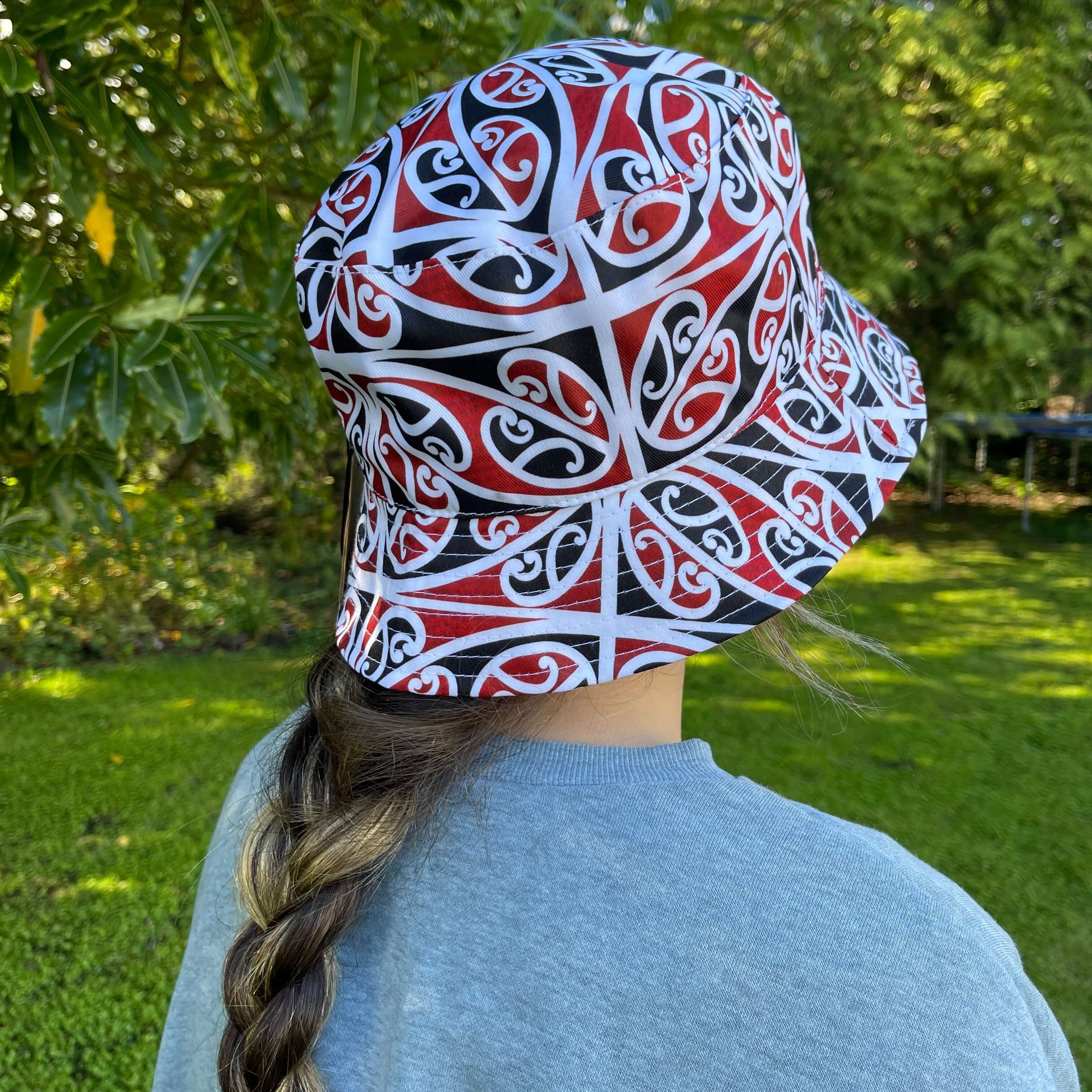 Girl wearing bucket hat with black, red & white maori koru design.