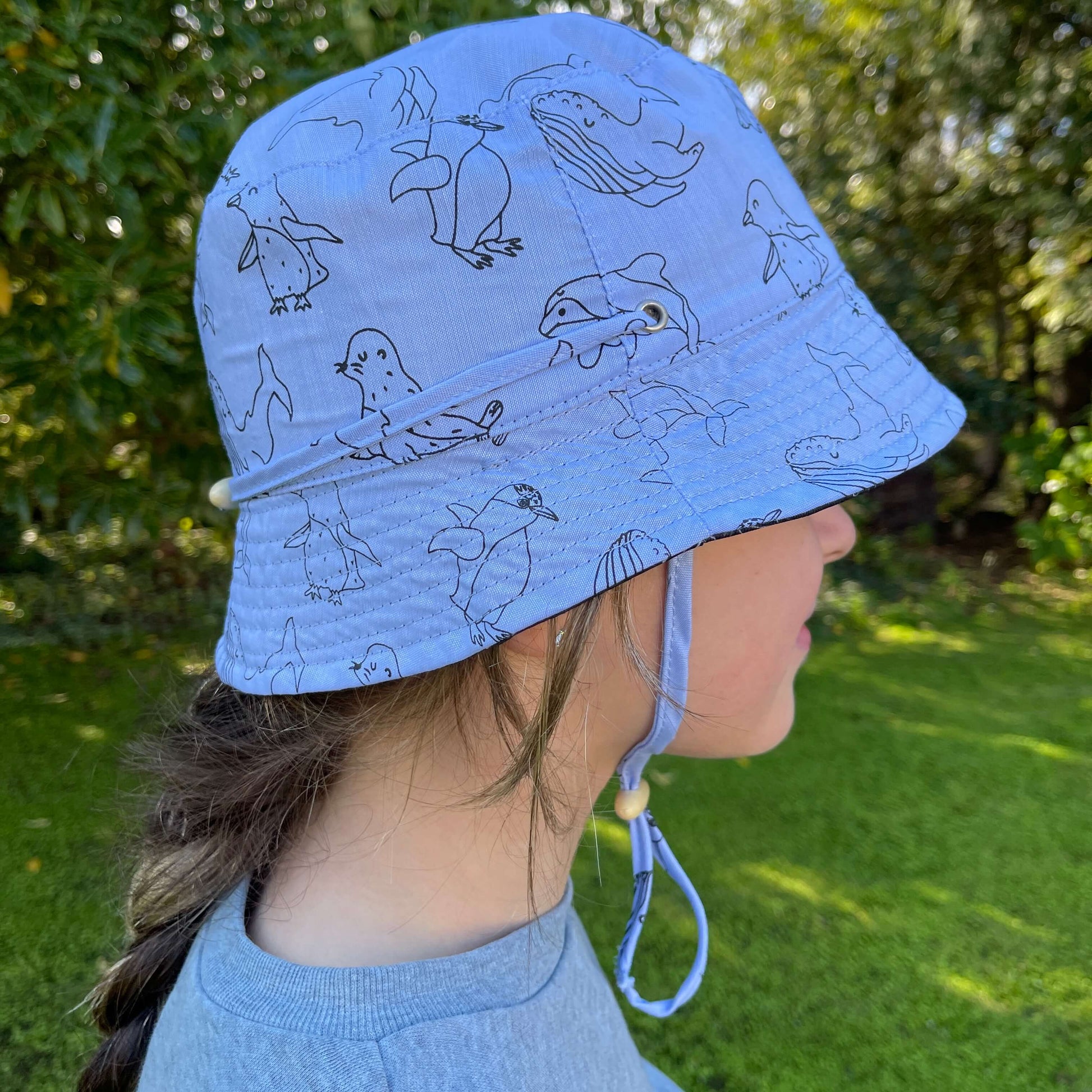 Girl wearing a bucket hat in denim blue with animal outlines in black and tied under the chin.