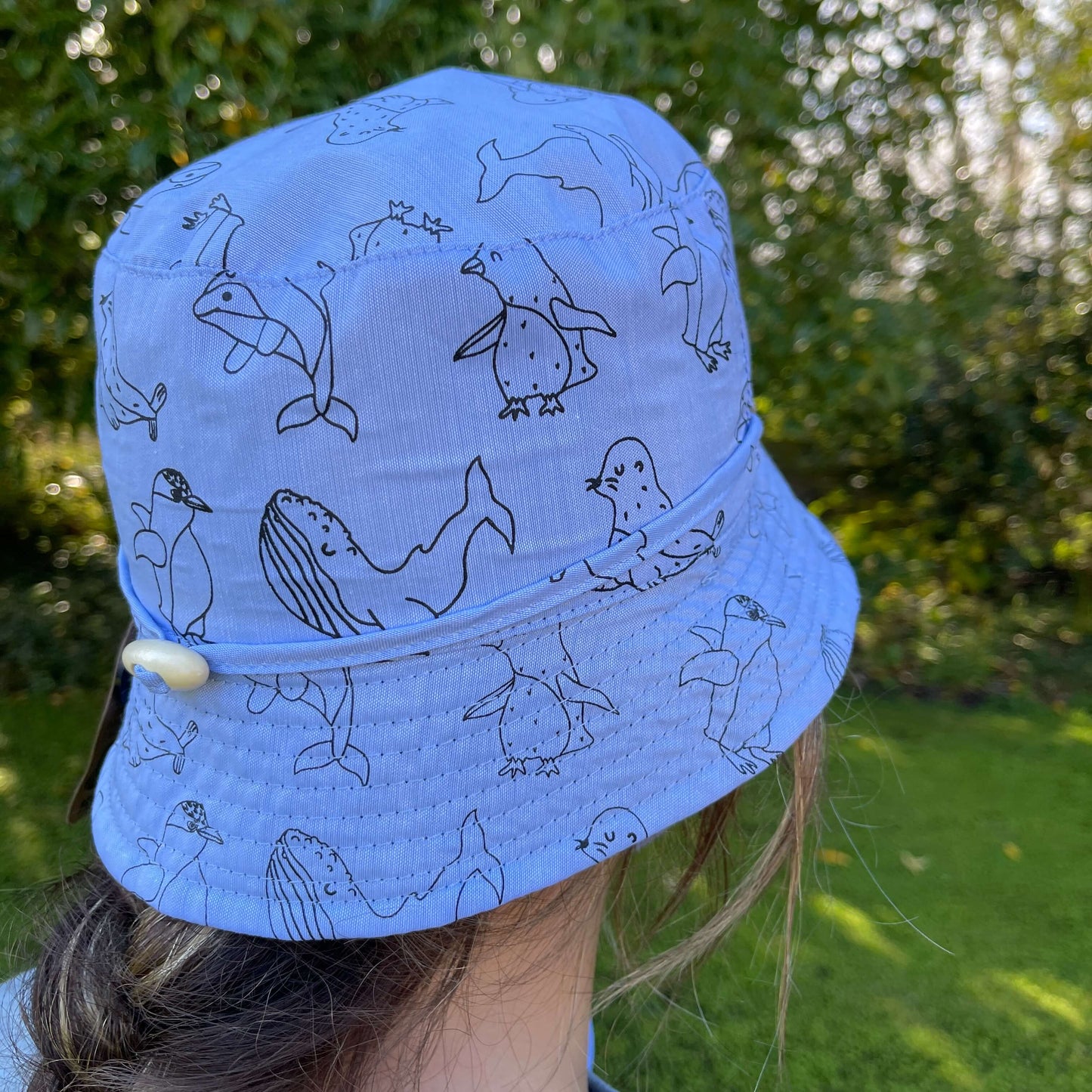 Girl wearing a bucket hat in denim blue with animal outlines in black.