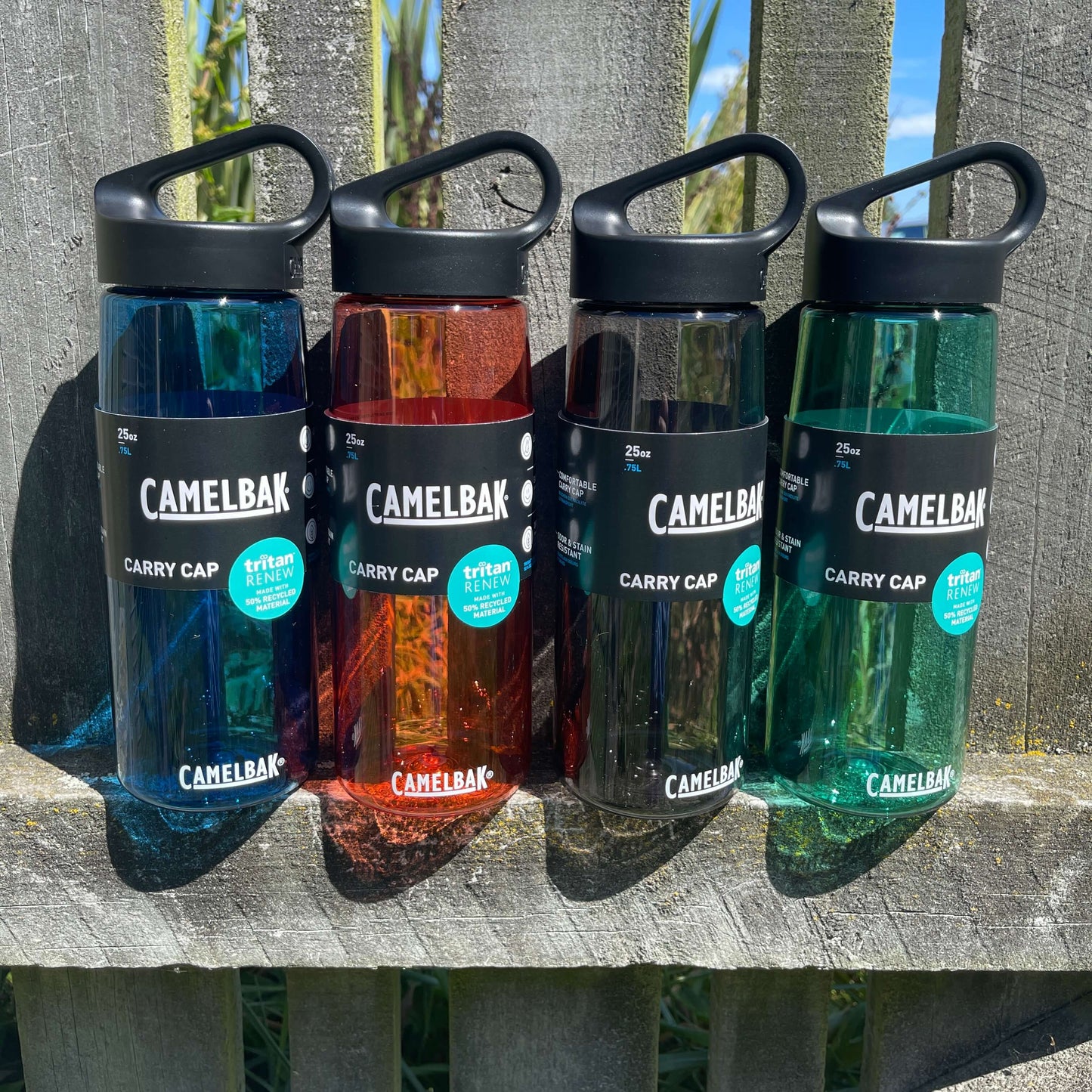 Group of four camelbak drink bottle in different colours lined up on a fence.