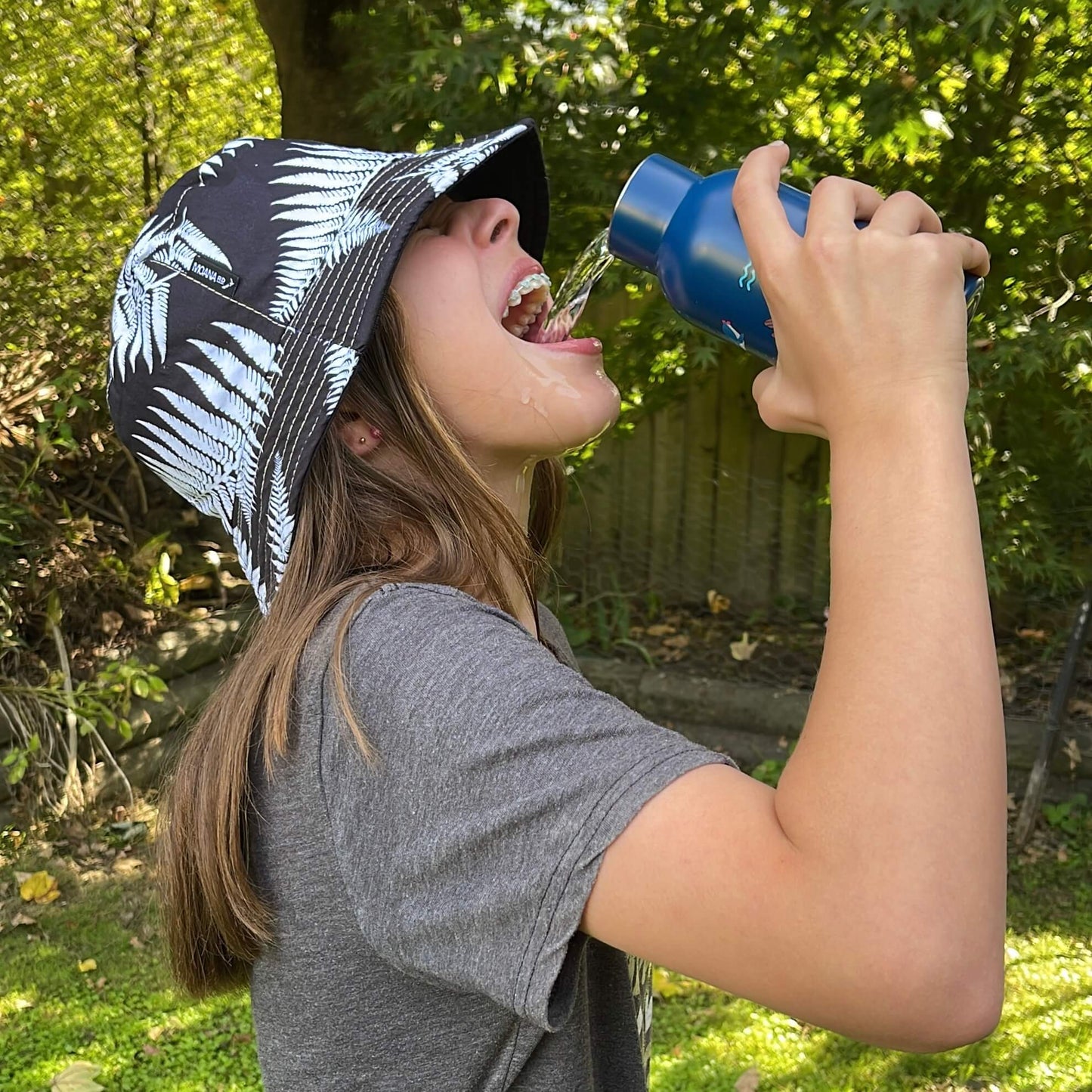 Young girl pouring water from a drink bottle into her mouth.