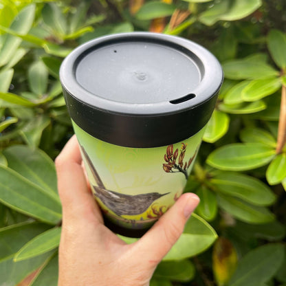 Black reusable coffee cup with Hihi birds and Flax flowers on a green background showcasing the lid with sipper hole.