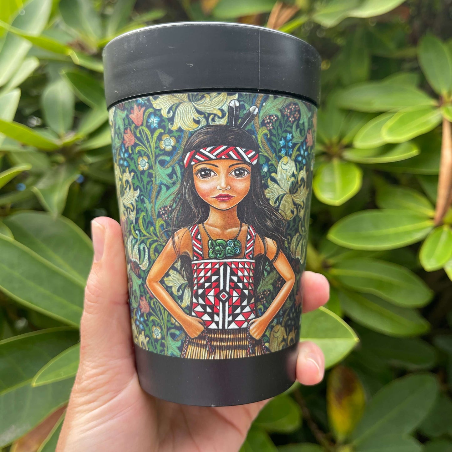 Black reusable coffee cup featuring a floral wrap and featuring an artists image of a young Māori girl.