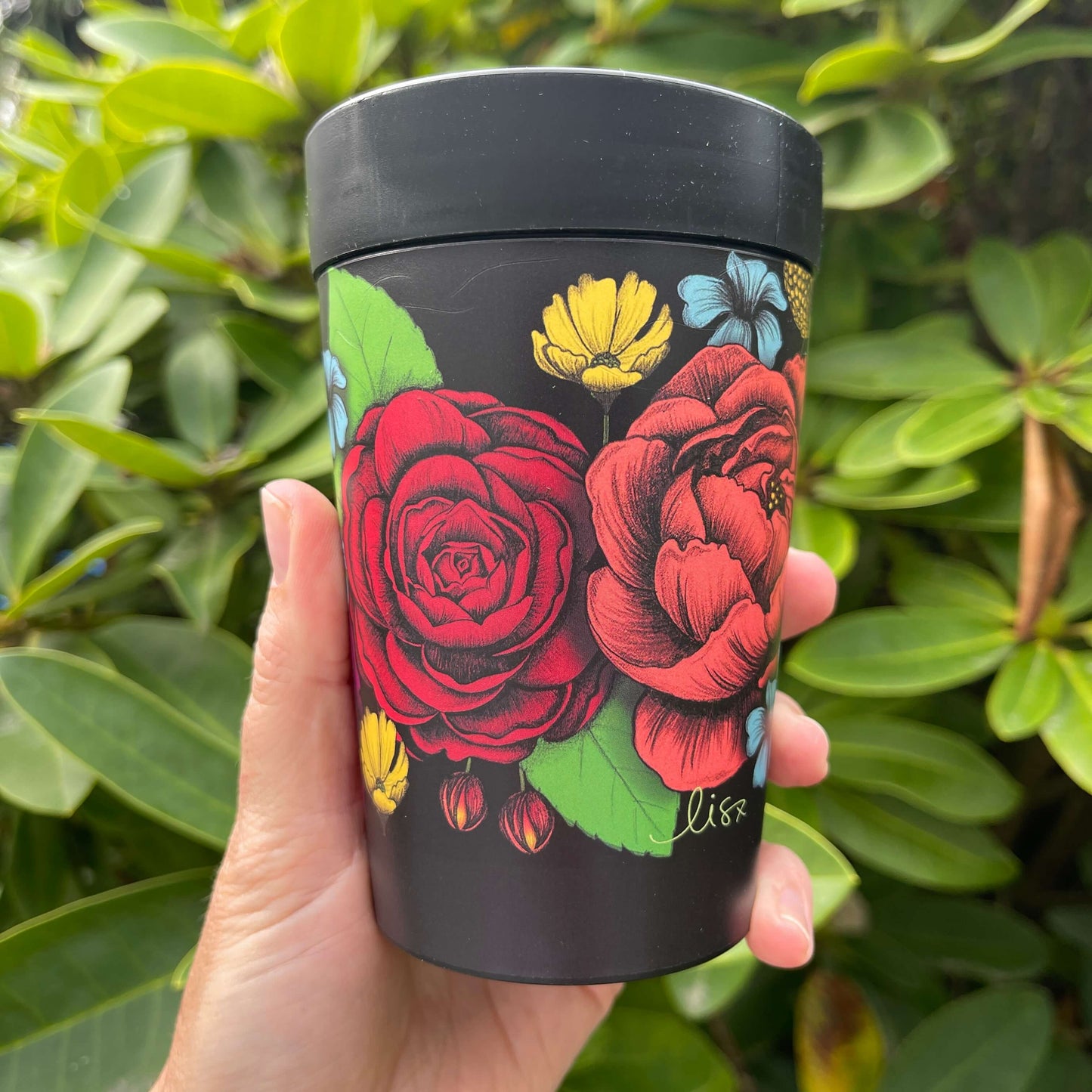 Black reusable coffee cup with bright bold flowers wrapped around it.
