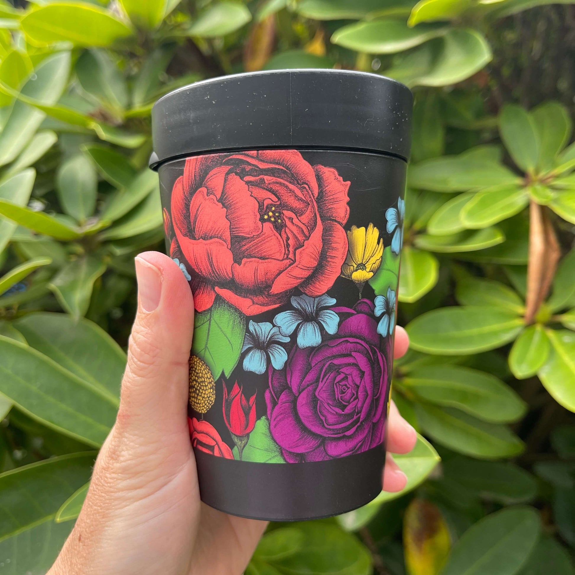 Black reusable coffee cup with bright bold flowers wrapped around it.
