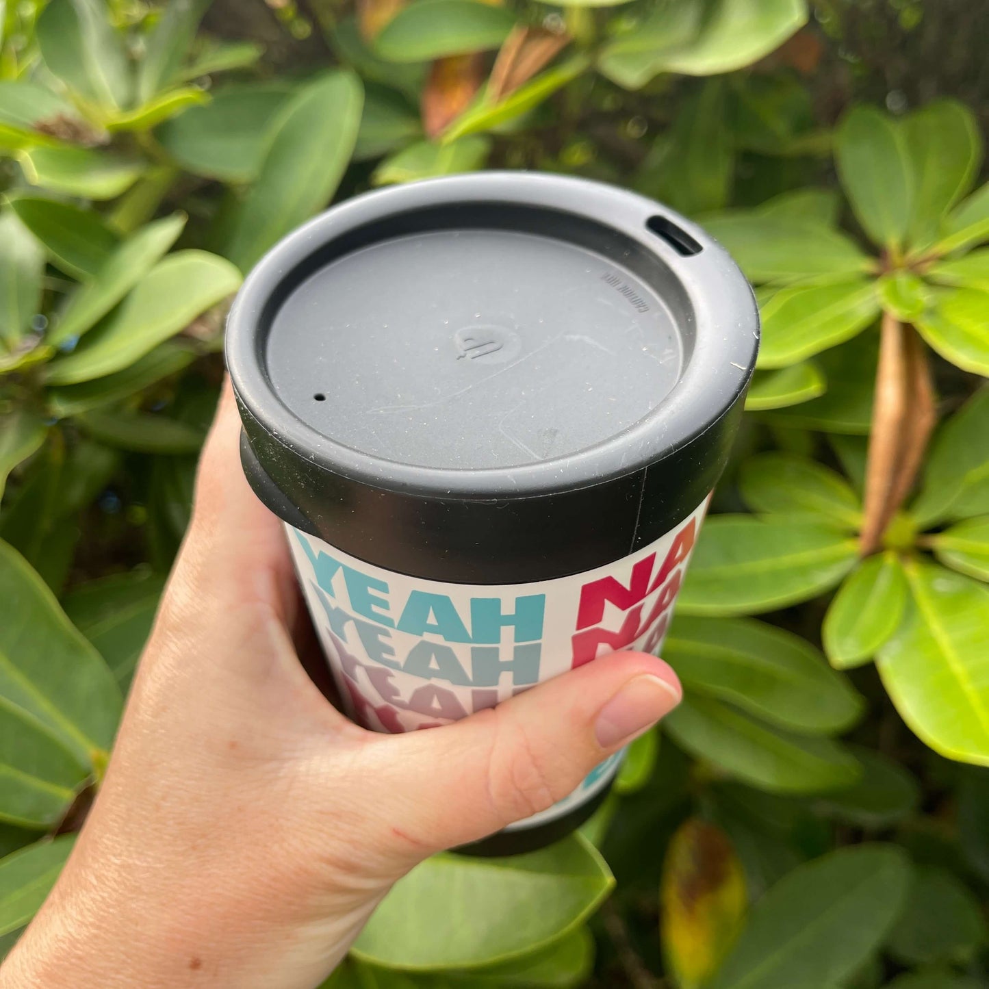Black reusable coffee cup highlighting the lid with sipper hole.