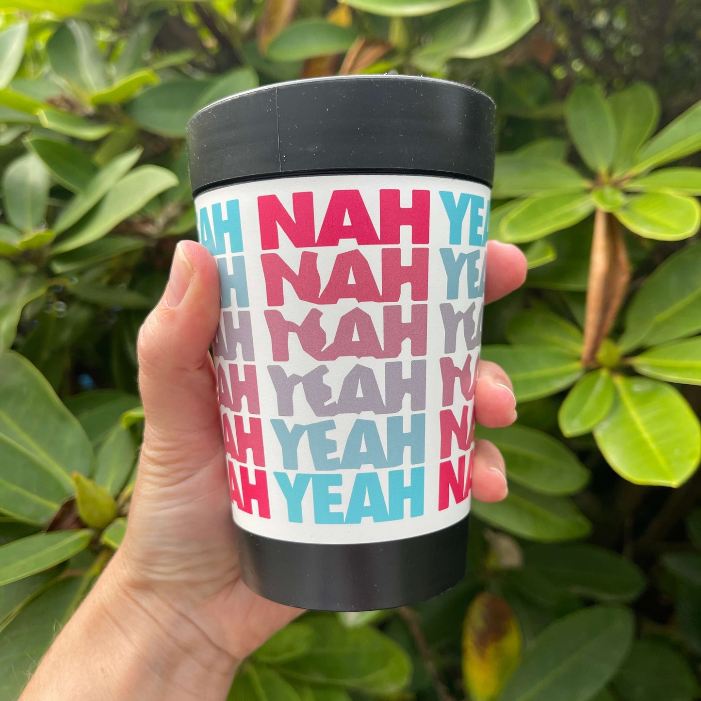 Black reusable coffee cup with white wrap and pink and blue words saying Yeah Nah.