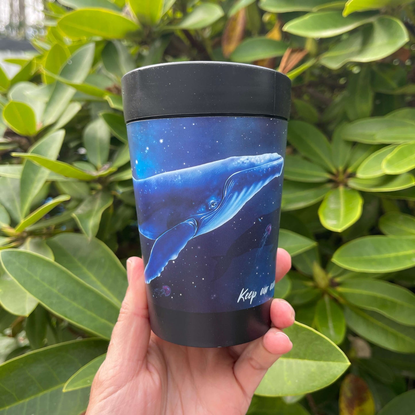 Black reusable coffee cup with blue galaxy wrap featuring a Humpback whale and the words "Keep our oceans beautiful".