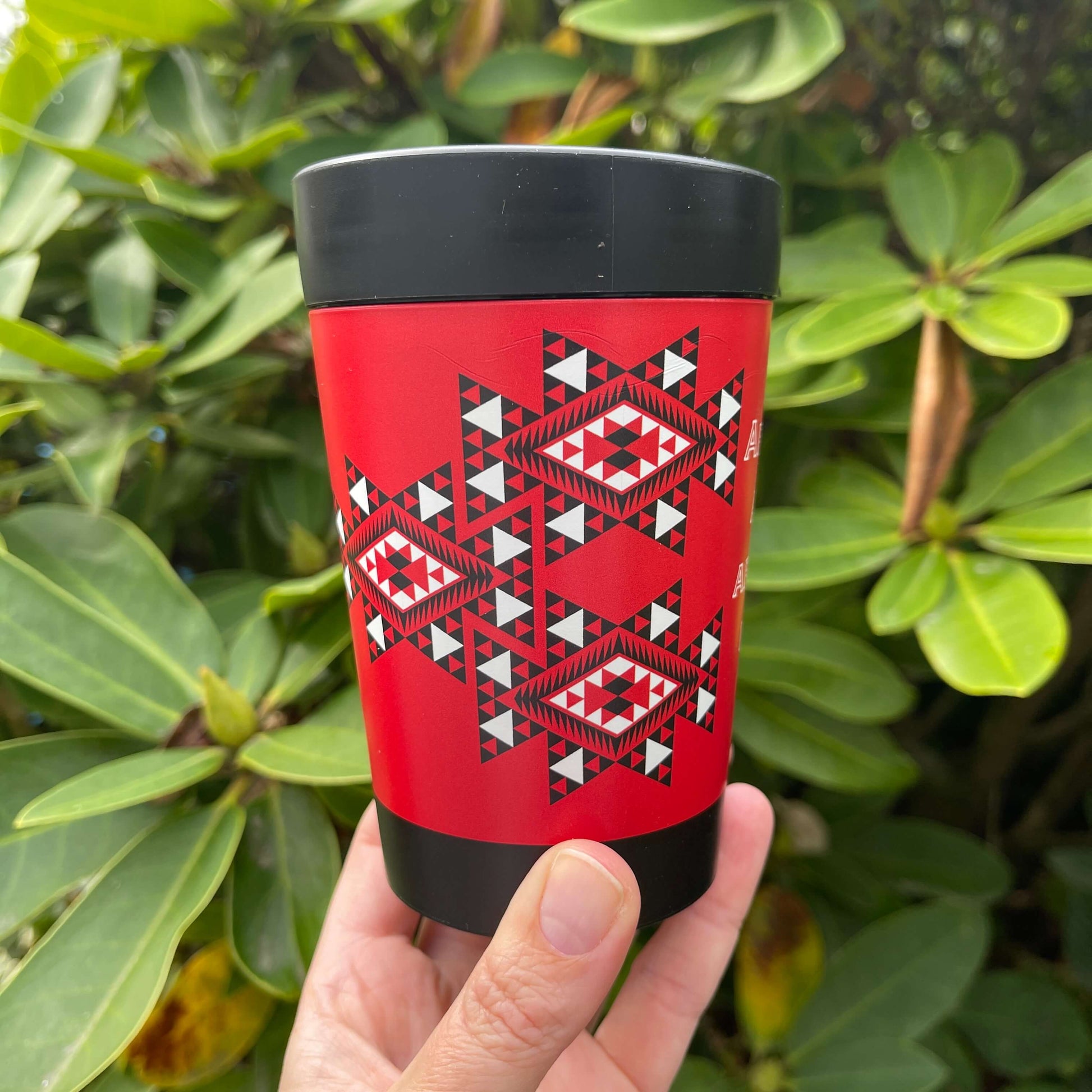 Reusable coffee cup in black with red, white and black wrapped image featuring Maori patterns.