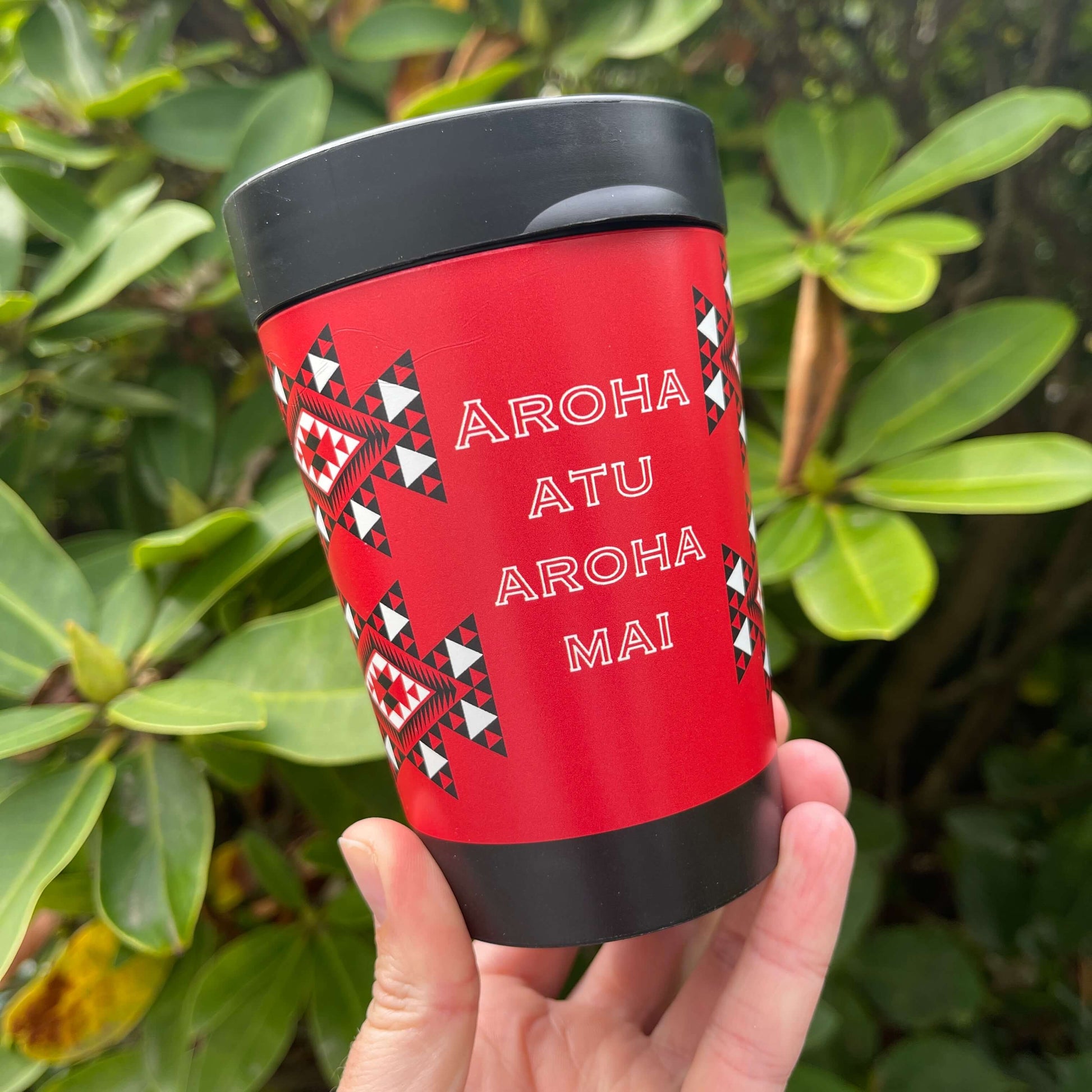 Reusable coffee cup in black with red, white and black wrapped image featuring Maori patterns and the words Aroha Atu Aroha Mai.