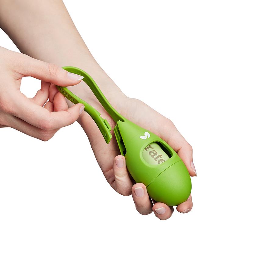 Bright green silicone tea drop shaped dog poo bag dispenser  with women's hands showing how the loop is removed to attach to a leash.
