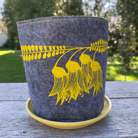 Grey felt planter with yellow kowhai flowers printed on it and sitting in a yellow dish.