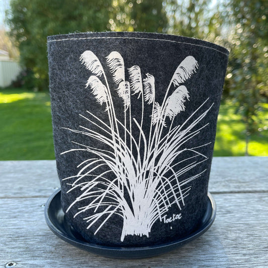 Dark grey felt planter with white toetoe plant printed on it sitting in a grey saucer.