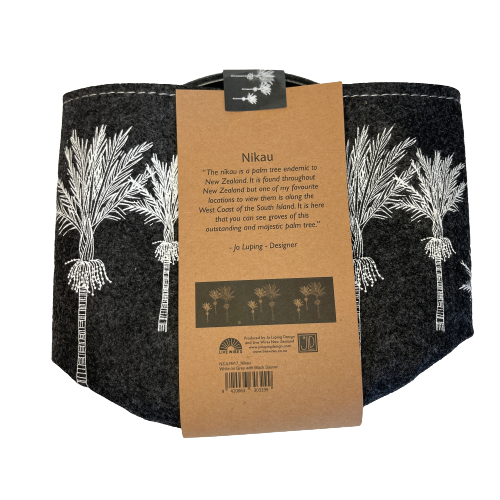 Dark grey felt planter with white Nikau trees printed on it sitting in a grey dish, flat packed and wrapped with kraft paper.