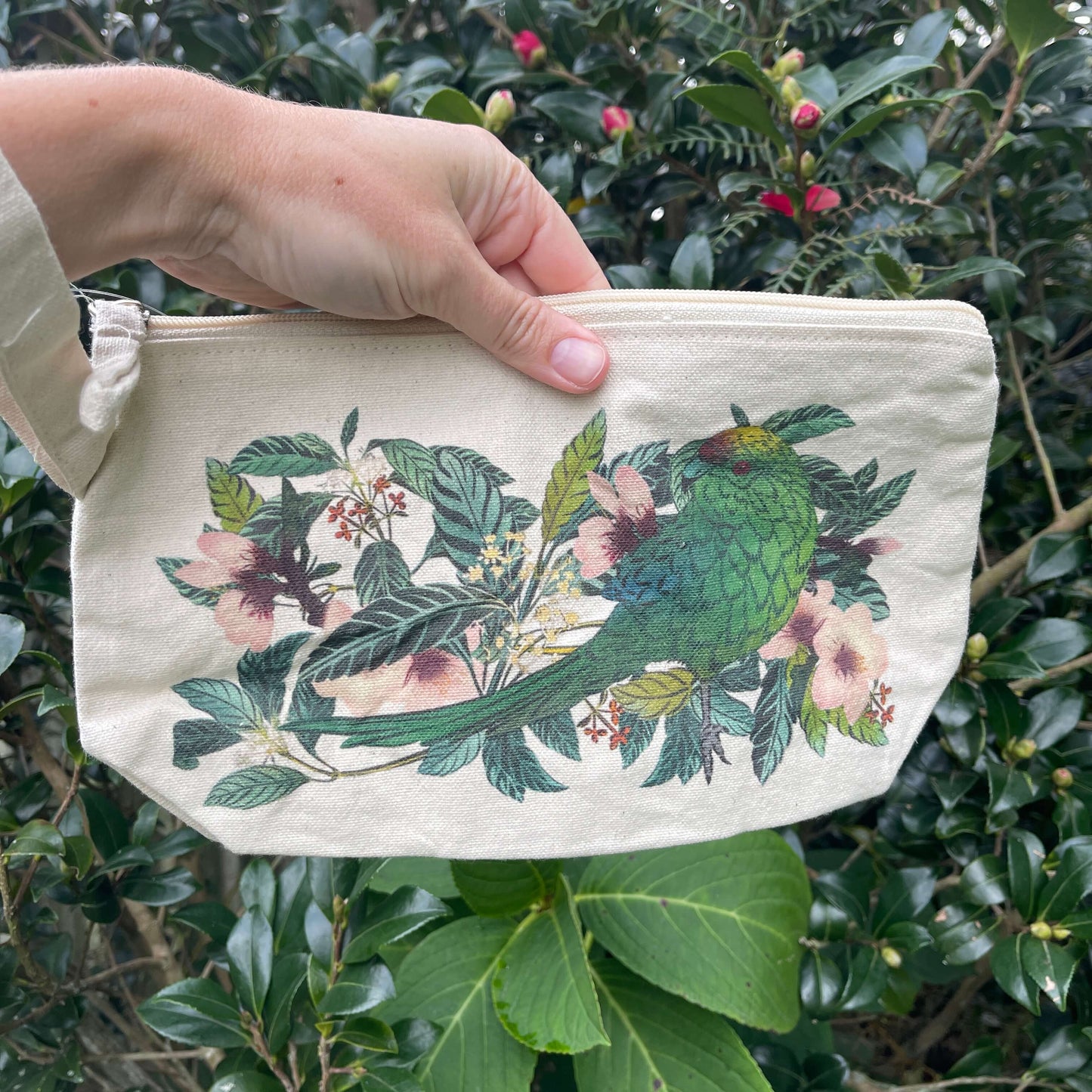 Womens hand holding a cotton clutch with vibrant Parakeet print.