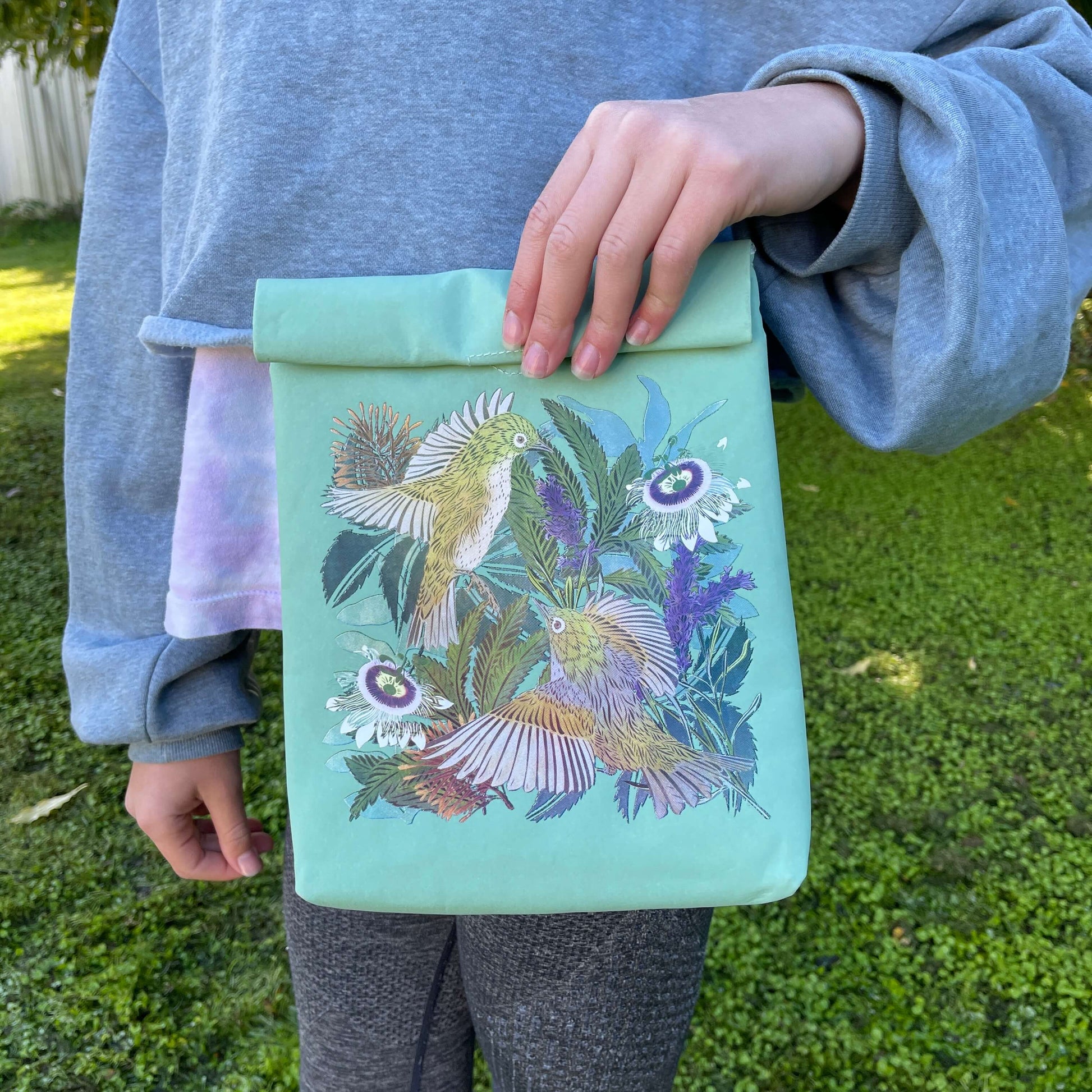 Person holding a light blue folding paper style lunch bag with floral and bird design.