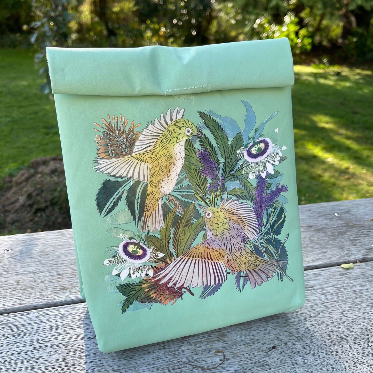 A light blue folding paper style lunch bag with floral and bird design.