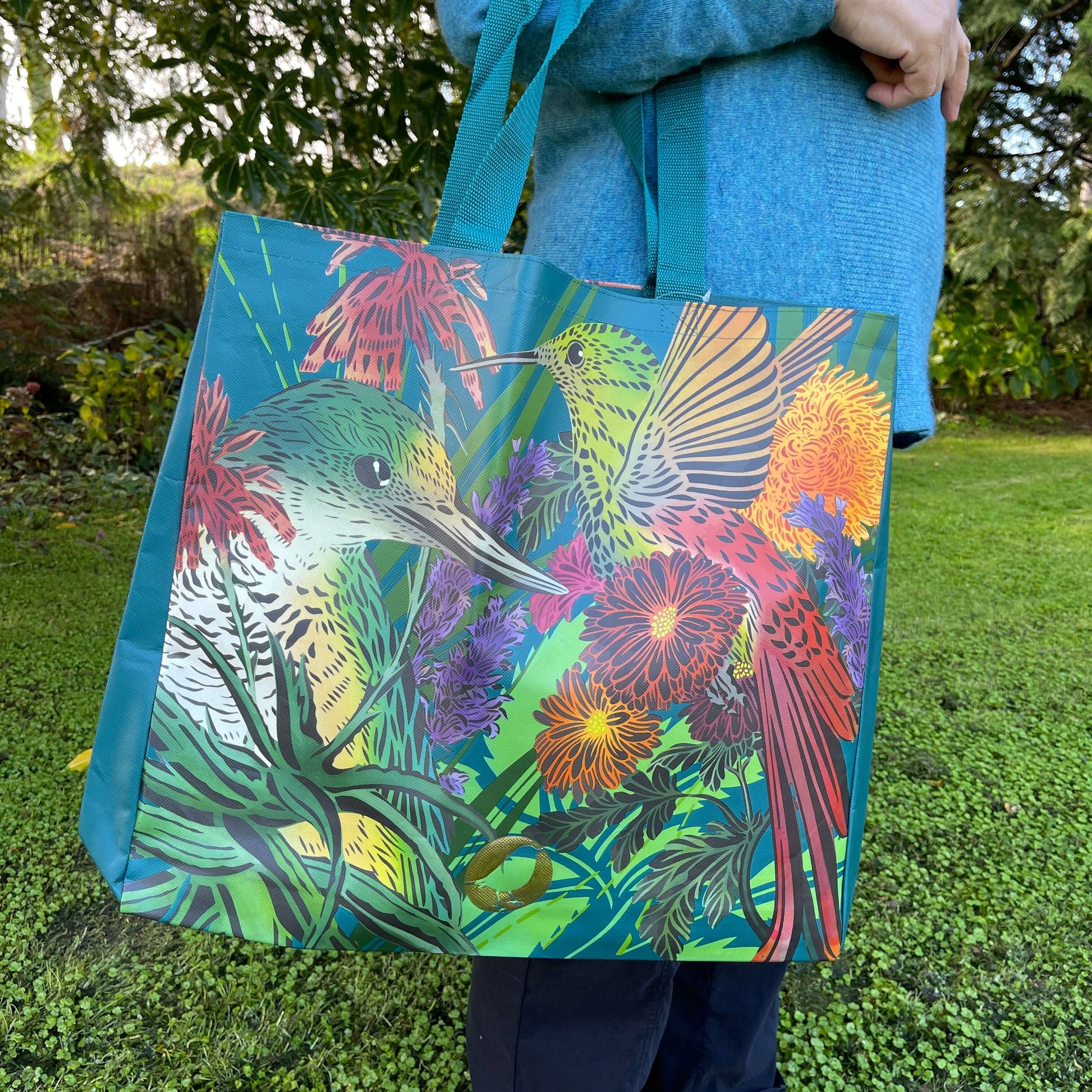 Woman with a tote bag over her arm. The vibrant coloured tote bag features birds & flowers by artist Flox.