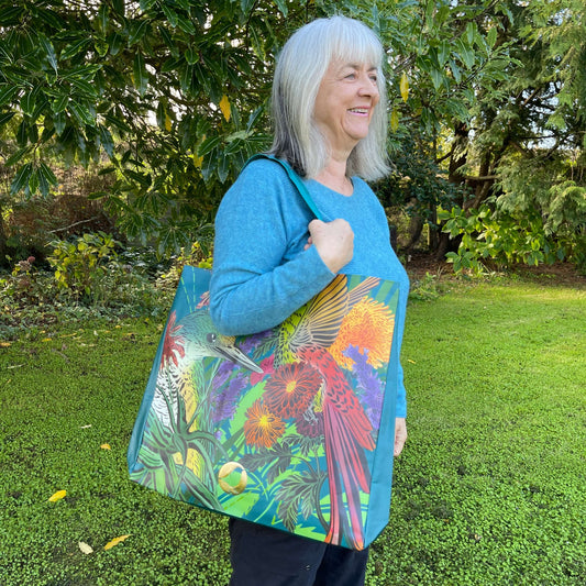 Woman with a tote bag over her arm. The vibrant coloured tote bag features birds & flowers by artist Flox.