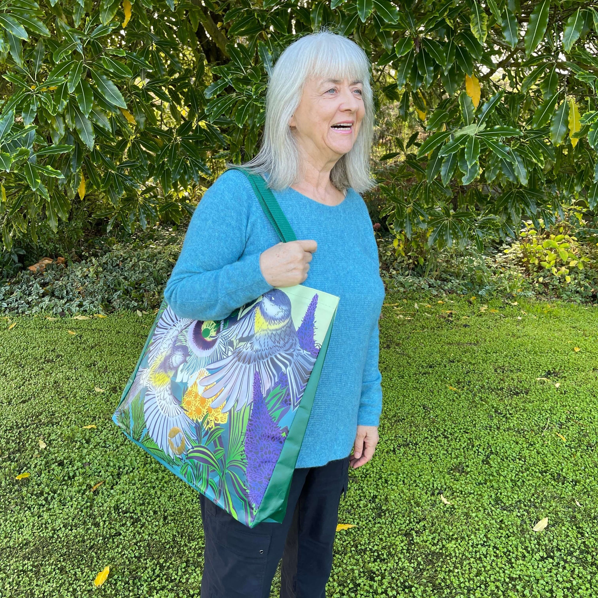 Woman with a tote bag over her arm. The vibrant coloured tote bag features Miromiro birds by artist Flox.