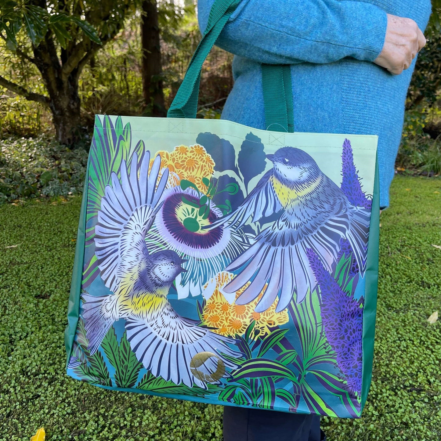 Woman with a tote bag over her arm. The vibrant coloured tote bag features Miromiro birds by artist Flox.