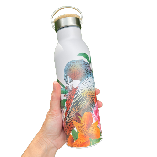 Womens hand holding a white drink bottle featuring artwork of a Kaka bird and flowers. Bottle has a stainless and wooden screw top with handle.