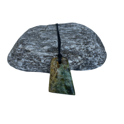 Greenstone freeform pendant on a black wax cord draped over a rock.