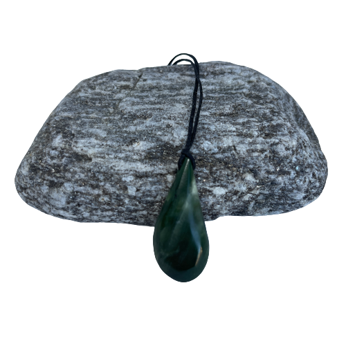 Greenstone freeform pendant on a black wax cord draped over a rock.