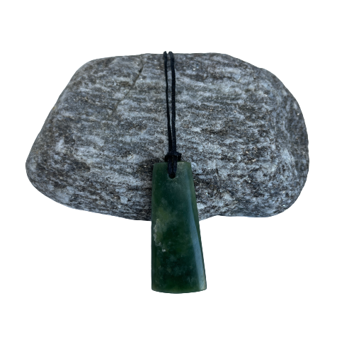 Greenstone freeform pendant on a black wax cord draped over a rock.