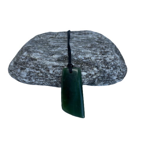 Greenstone freeform pendant on a black wax cord draped over a rock.