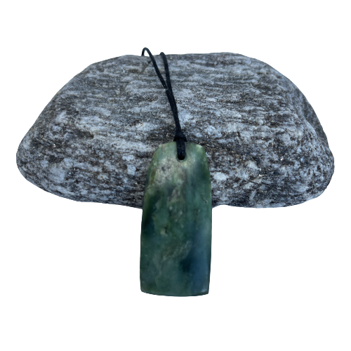 Greenstone freeform pendant on a black wax cord draped over a rock.