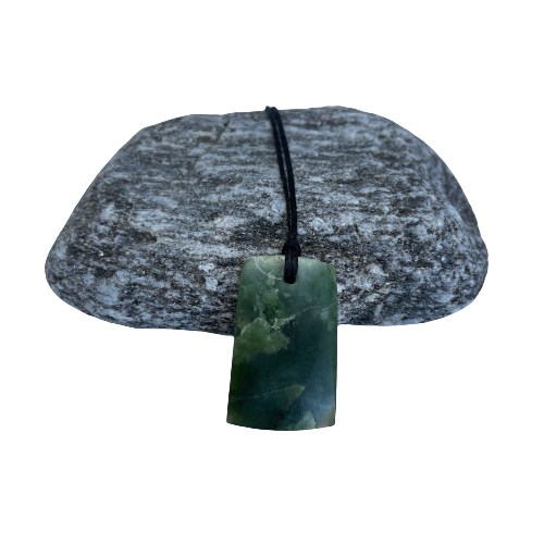 Greenstone freeform pendant on a black wax cord draped over a rock.