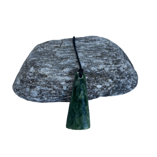 Greenstone freeform pendant on a black wax cord draped over a rock.