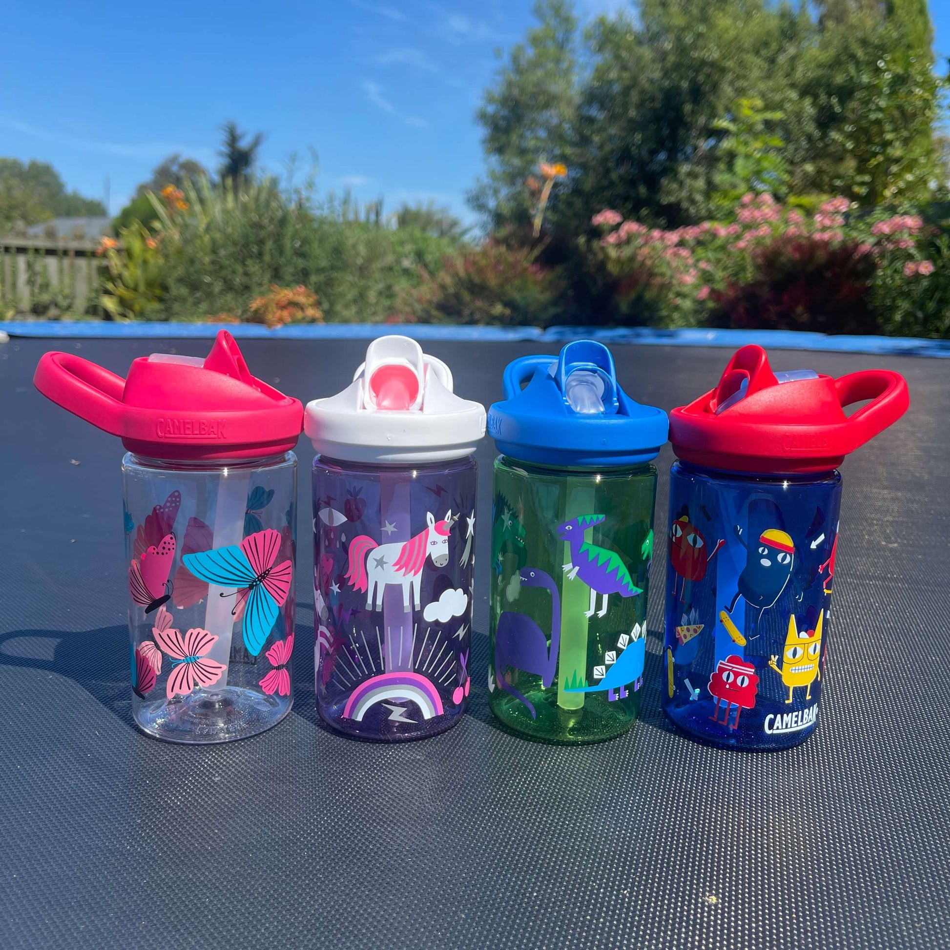 Four kids bright colourful drink bottles on a trampoline.