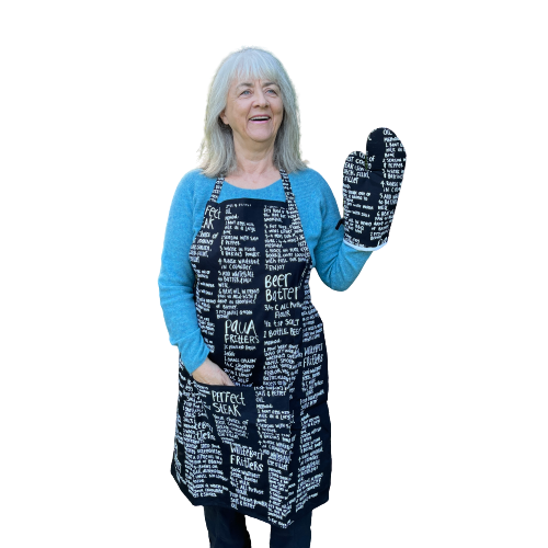 Woman wearing a black apron and mitt set featuring recipes printed on it.