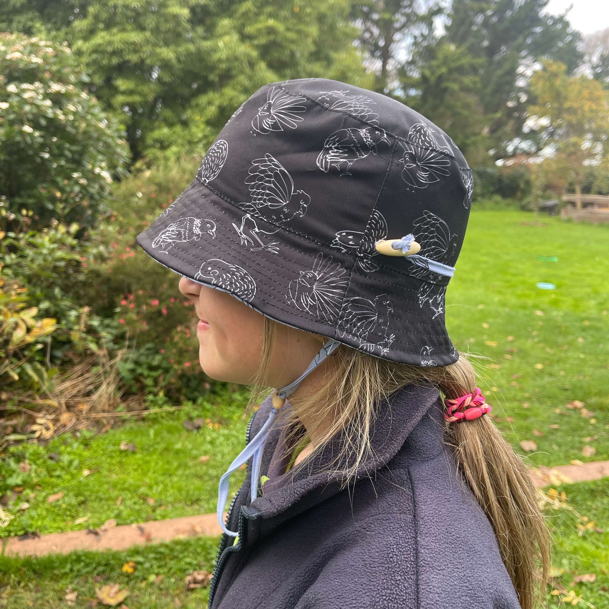 Girl wearing a black bucket hat with white outlines of NZ birds.