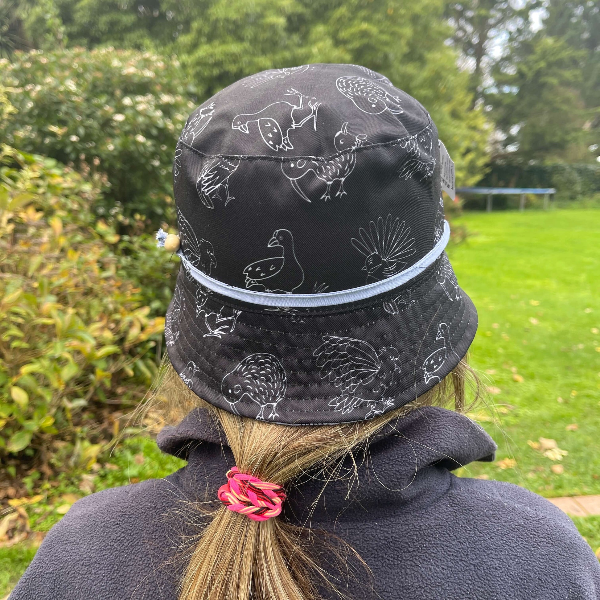 Girl wearing a black bucket hat with white outlines of NZ birds.