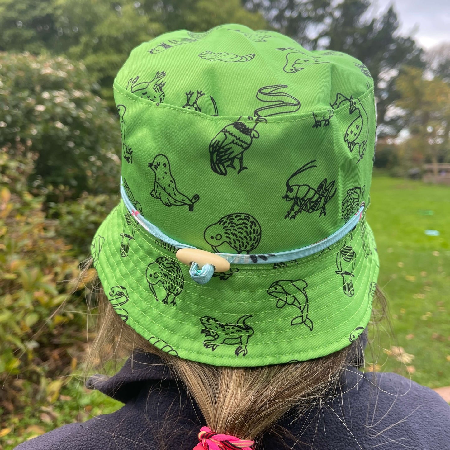 Girl wearing a Bright green bucket hat with black outlines of Native New Zealand animals.
