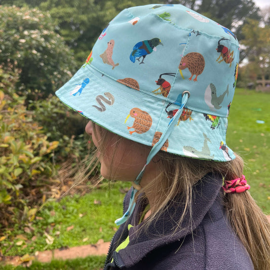 Girl wearing a light blue bucket hat with native New Zealand animals printed on it.