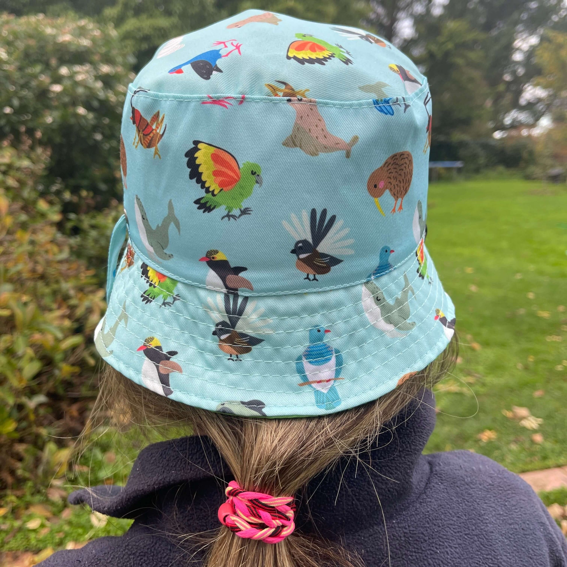 Girl wearing a light blue bucket hat with native New Zealand animals printed on it.