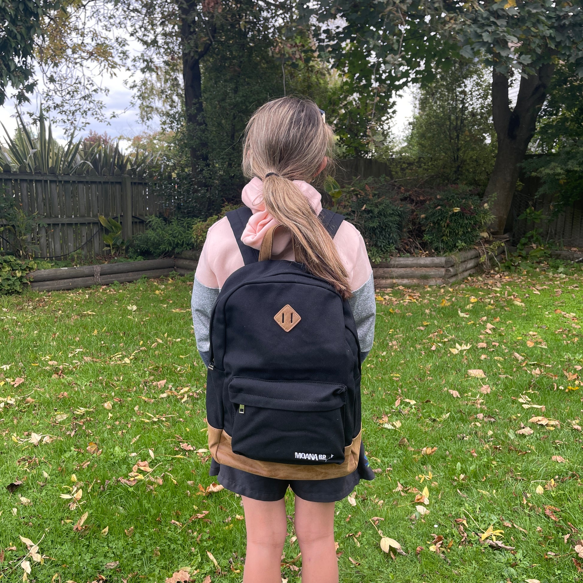 Girl wearing black & tan backpack with 2 zippered compartments.