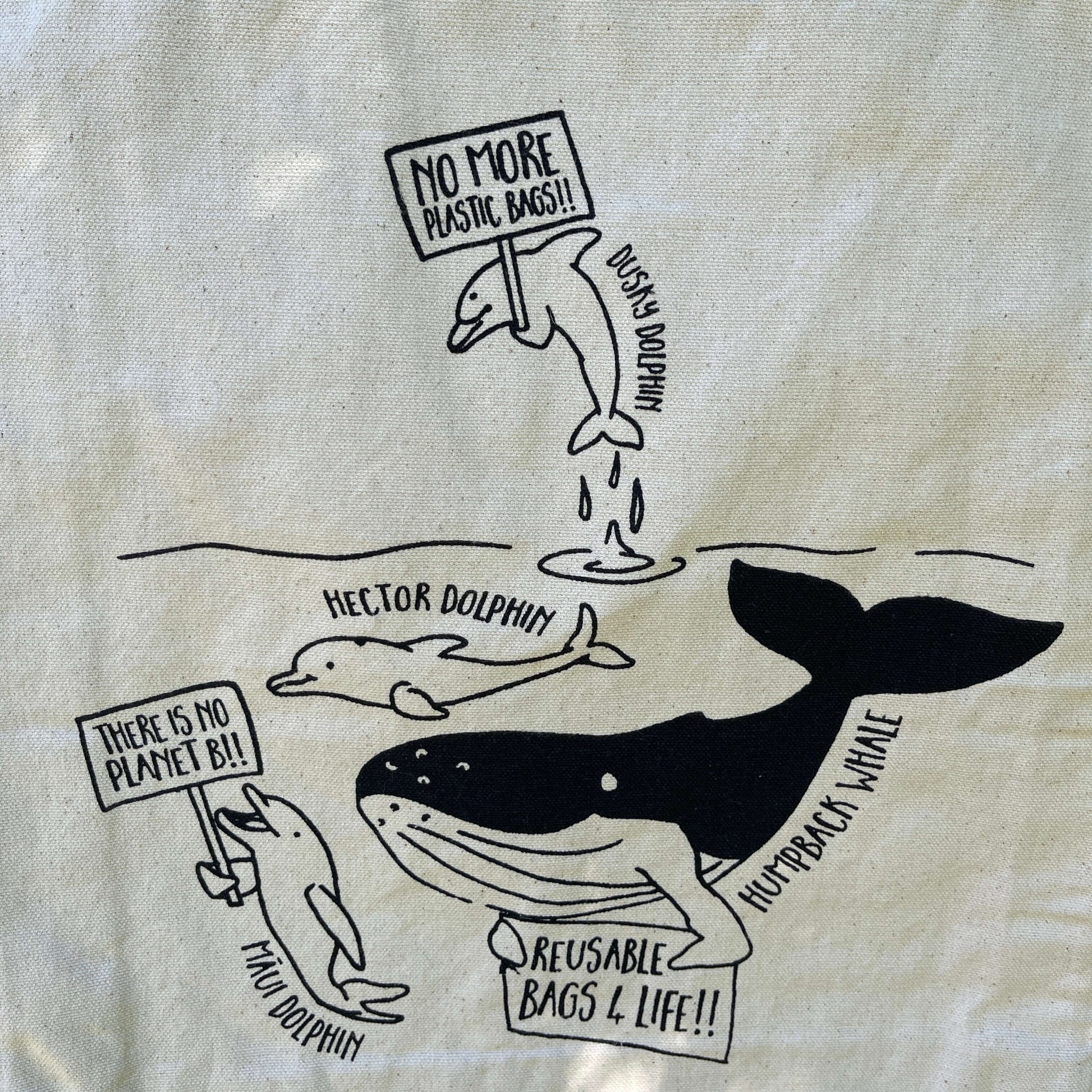 White canvas tote bag with whales and dolphins in black print protesting about plastic use.