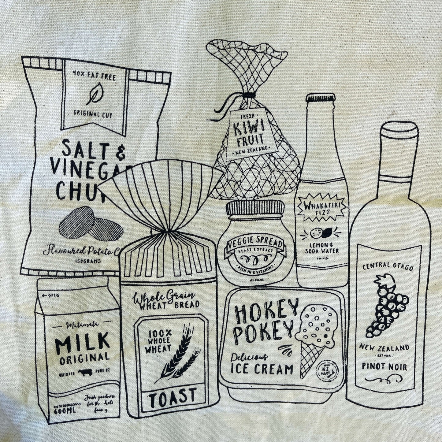 Canvas tote bag with black ink print of various Kiwi grocery staples such as bread, wine & hokey pokey ice cream.