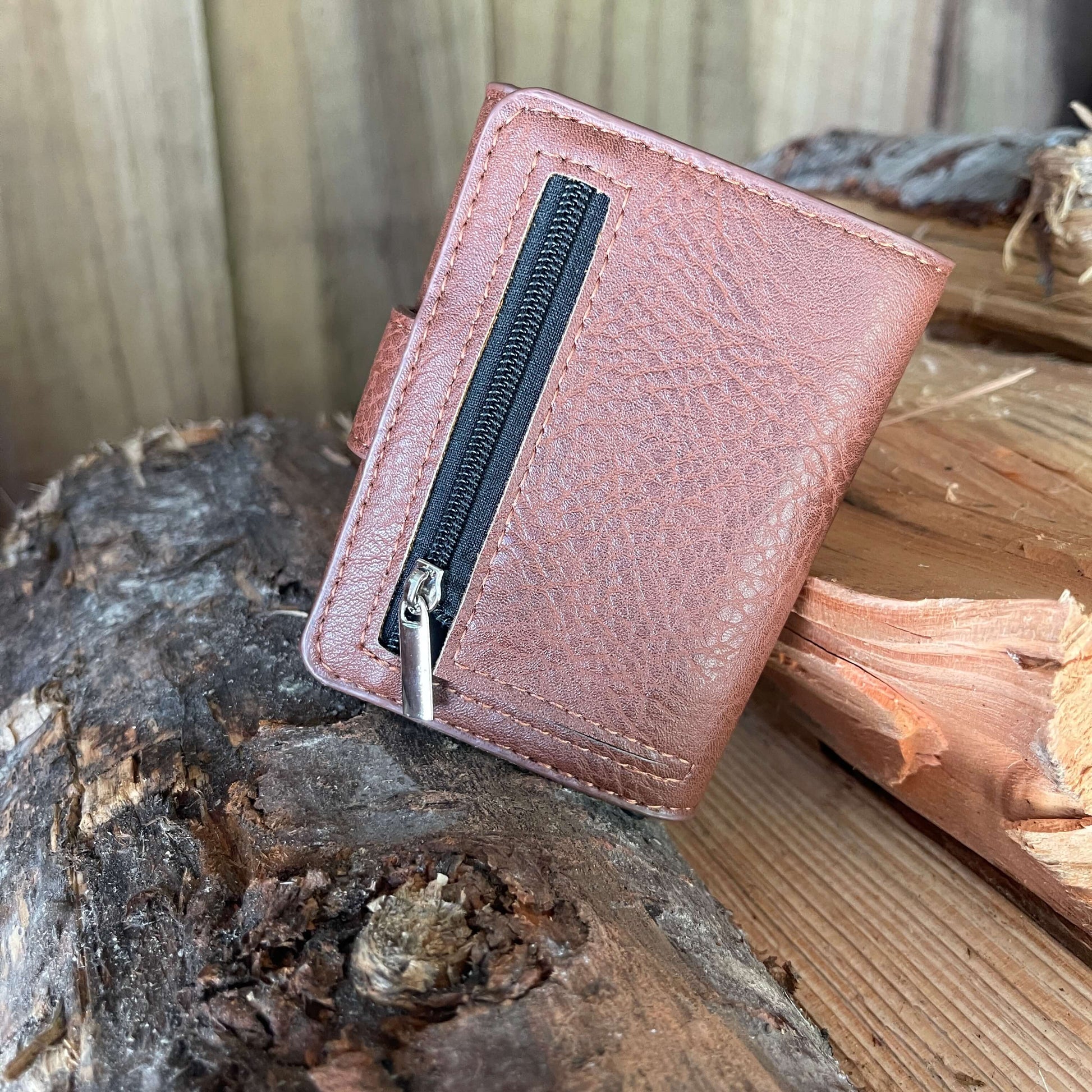 Small pocket wallet in tan sitting on a piece of firewood showing the back where the zippered coin pocket is.