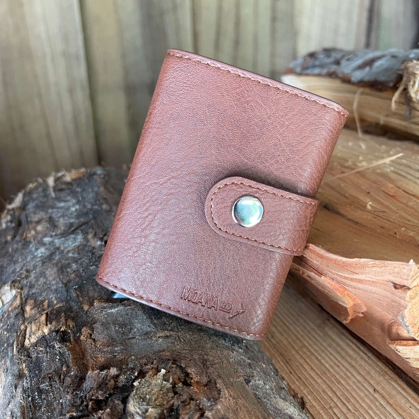 Small pocket wallet in tan sitting on a piece of firewood.