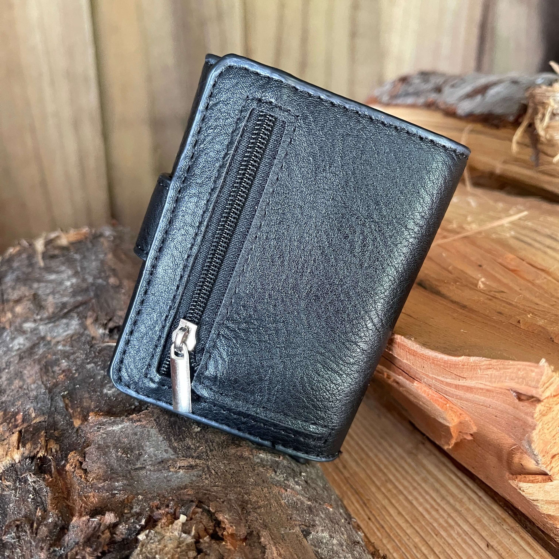 Small pocket wallet in black sitting on a piece of firewood showing the back where the zippered coin pocket is.