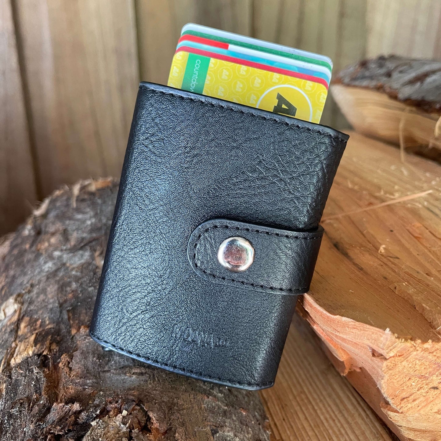 Small pocket wallet in black sitting on a piece of firewood showing how the cards pop out.