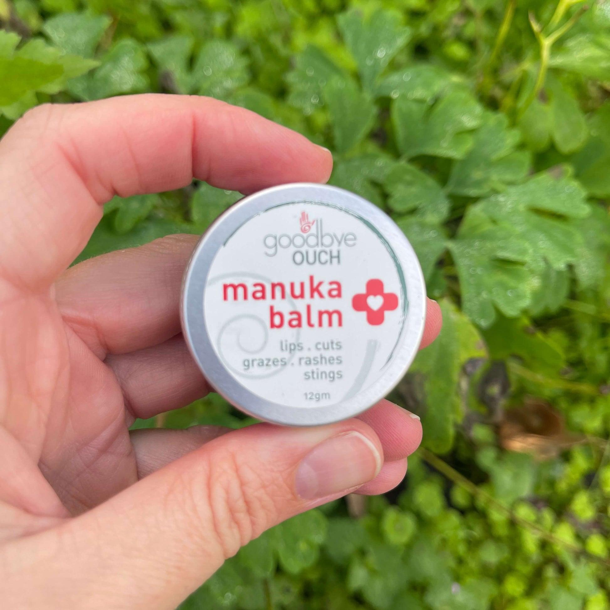 Persons hand holding a small tin of Manuka Balm by Goodbye Ouch.
