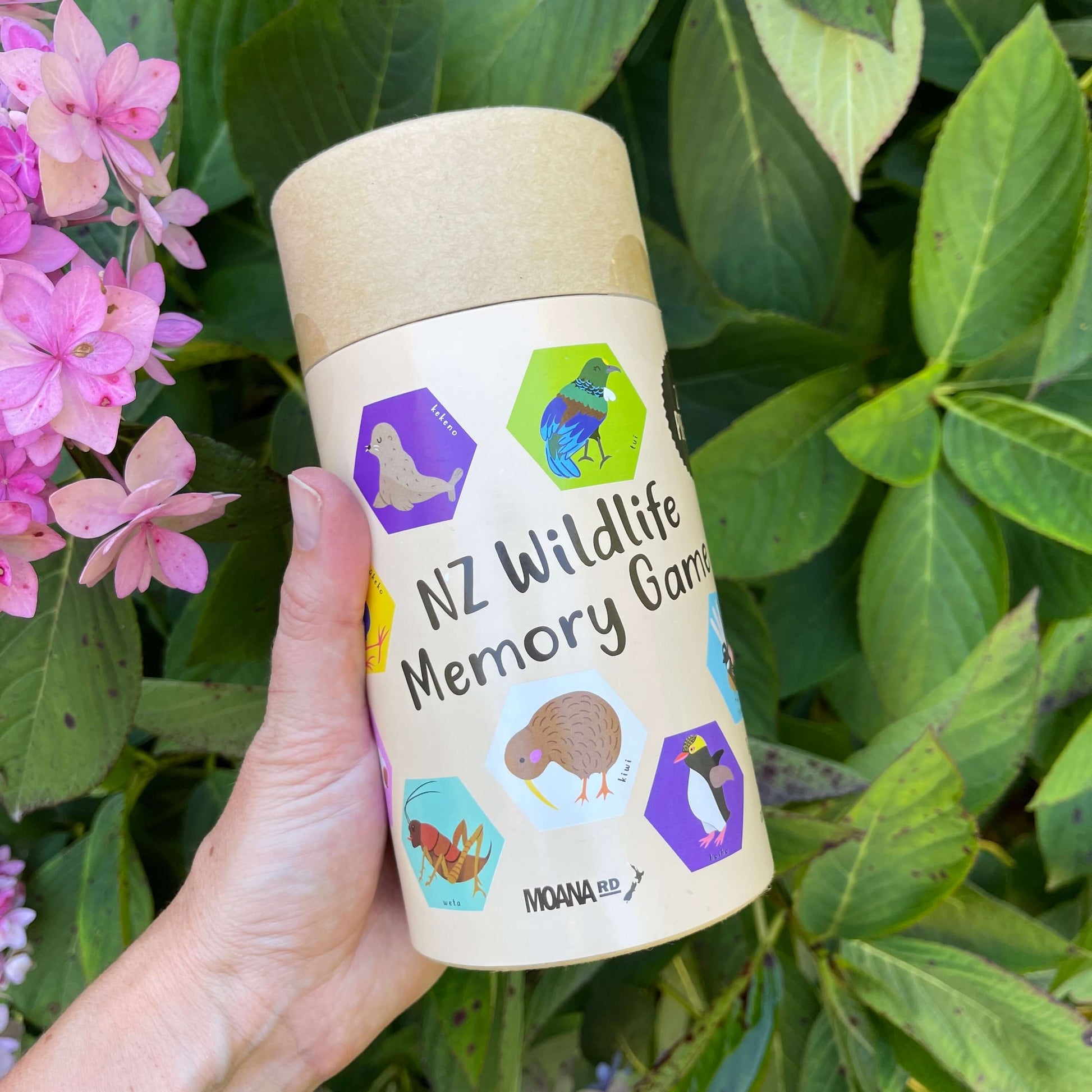 Women's hand holding cardboard tube with an NZ Wildlife Memory Game inside.